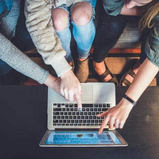 three people pointing at the screen of a laptop