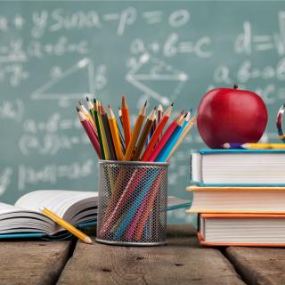 books, pencils on a desk with a green board in the background