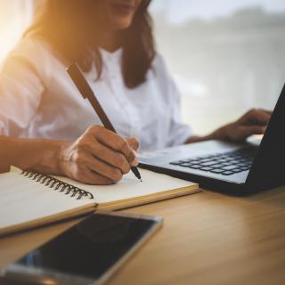 Woman writing down while working on laptop Woman writing down while working on laptop